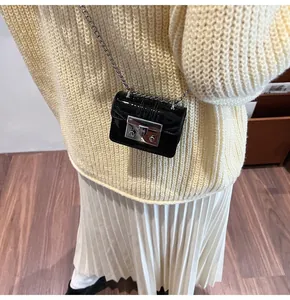 Close-up of mini black patent leather crossbody bag with silver lock on a knit sweater