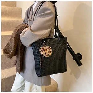 Detail of black woven tote bag with a leopard print heart charm and sleek shoulder straps