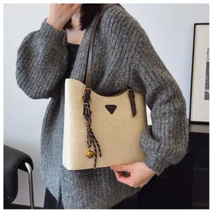 Détail d'un sac cabas blanc cassé avec logo triangulaire et breloque cloche tressée