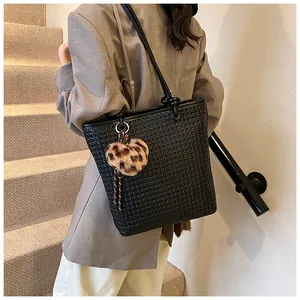 Close-up of woven black tote bag featuring a leopard print heart charm and knot strap