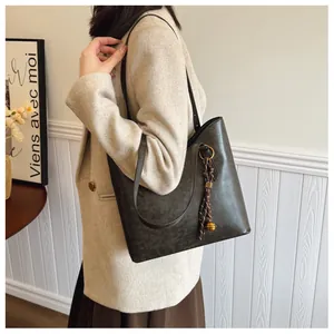 Détail d'un grand sac cabas gris foncé avec pendentif clochette en métal et texture similicuir