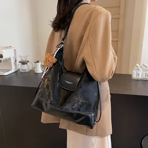 Chic black leather tote bag with vintage texture and cute brown teddy bear charm accessory