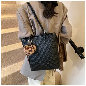 Close-up of black woven tote bag with a leopard print heart charm worn on the shoulder