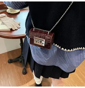 Close-up of wine red patent leather mini crossbody bag with silver chain on a wooden table