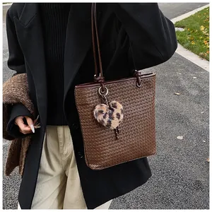 Detail of dark brown woven tote bag with a leopard print plush heart charm and slim strap
