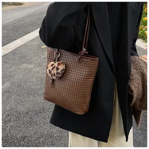 Detail of woven brown tote bag featuring leopard heart charm and slim shoulder straps