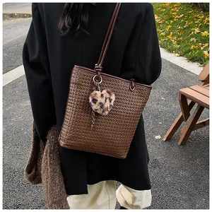 Brown woven tote bag detail with leopard print heart charm in an outdoor setting