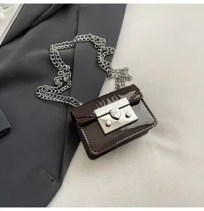 Detail of dark brown patent leather mini bag with silver metal buckle and chunky chain