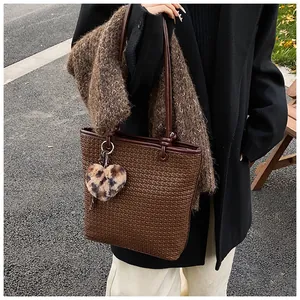 Brown woven tote bag with leopard heart charm worn by model in outdoor setting
