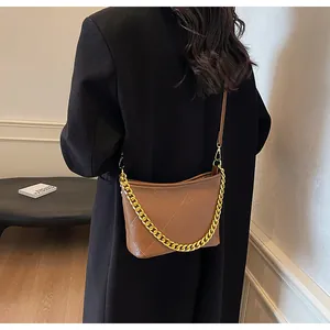Detail einer braunen Stepptasche mit goldener Kette, getragen von einem Modell innen