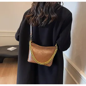 Detail einer braunen gesteppten Hobo-Tasche aus Leder mit goldener Gliederkette am Model