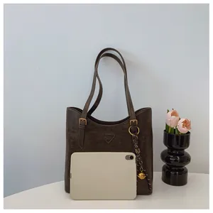 Détail d'un sac cabas marron foncé avec bandoulière réglable et breloque dorée