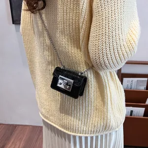 Glossy black mini crossbody bag with silver buckle and metal chain strap worn by model