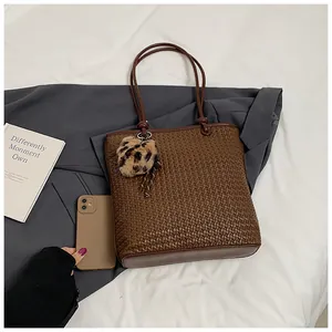 Detail of deep brown woven tote bag featuring a leopard faux fur pompom charm accessory