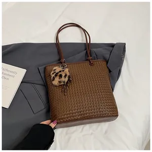 Detail of dark brown woven tote bag featuring handle knots and leopard heart charm
