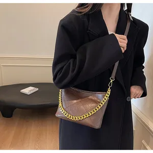 Detail der dunkelbraunen gesteppten Beuteltasche mit goldener Kette auf Wollmantel