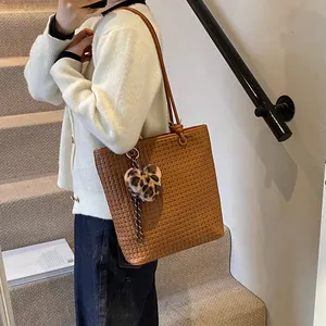 Brown woven tote bag with slim straps and leopard heart pendant for daily wear