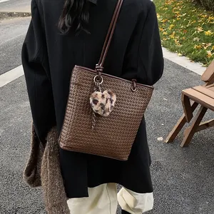 Brown woven tote bag with leopard heart charm and long shoulder strap in autumn setting