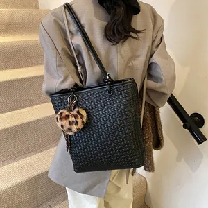 Woven black tote bag with leopard heart charm worn over a grey blazer for a modern look