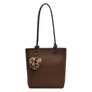 Dark brown woven tote bag with slim straps and a leopard heart charm pendant