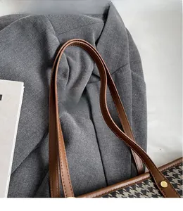 Detail of brown leather double straps and houndstooth fabric with gold rivets on tote bag