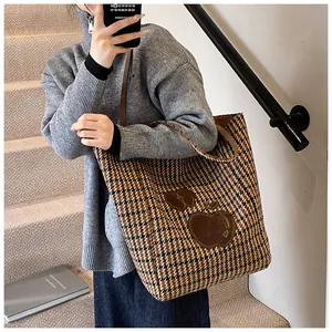 Gedetailleerd zicht op de grote houndstooth draagtas met appel-patch op de schouder