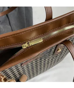 Detail of the houndstooth tote bag featuring smooth gold metal zipper and fashion leather tag
