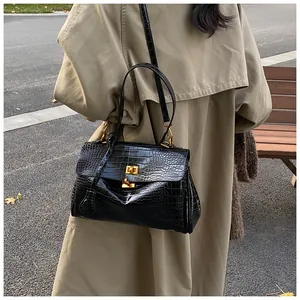 Dettaglio borsa nera a coccodrillo con fibbia dorata abbinata a un trench coat color kaki