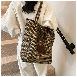 Detailopname van de houndstooth-tas met bruine leren appelpatch aan de schouder