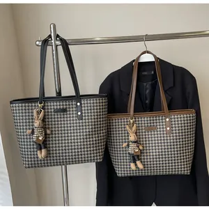 Detail of houndstooth tote bag featuring a metal logo plate and cute bunny charm pendant