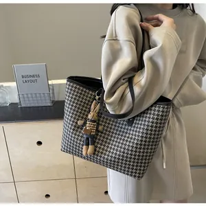 Close-up of houndstooth tote bag with plush rabbit pendant and faux leather strap