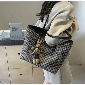 Detail of large houndstooth tote bag featuring black leather trim and a cute bunny charm