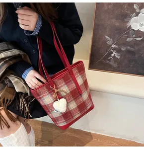 Détail du sac cabas en tweed à carreaux rouges avec poignées en cuir et breloque en cœur