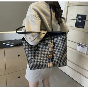 Detail of houndstooth tote bag showing leather straps and brown rabbit doll charm accessory