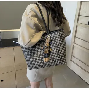 Detail view of large houndstooth tote bag with plush bunny charm worn on shoulder