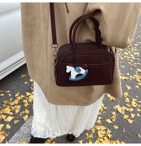 Detail of small brown leather bag with horse charm and adjustable strap on autumn leaves