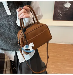 Close-up of brown leather crossbody bag featuring dual handles and a horse pendant detail