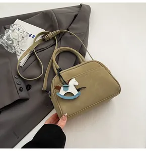 Detail view of khaki Boston crossbody bag with a cute rocking horse charm pendant