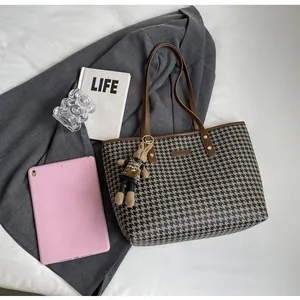Detail of houndstooth tote bag with brown straps and cute rabbit charm on gray blazer