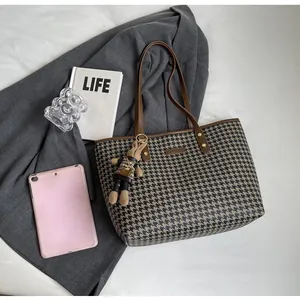 Detail of houndstooth tote bag with brown leather strap and decorative bunny charm