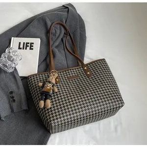 Detail of houndstooth tote bag featuring a cute bunny charm and brown leather handles