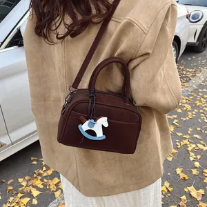 Brown faux suede Boston crossbody bag with horse pendant on autumn leaves backdrop