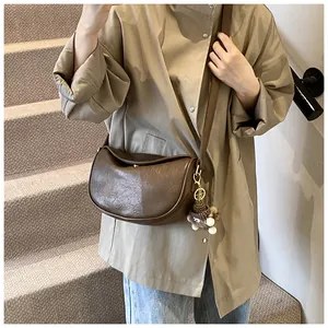 Brown leather crescent bag detail with a cute plush bear pendant on wide strap