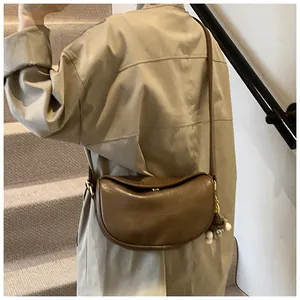 Detailed view of a vintage brown half-moon crossbody bag with a plush charm on a model