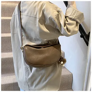 Brown faux leather half-moon shoulder bag with plush ball charm shown on a model