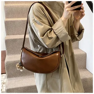 Close-up of a brown crescent shoulder bag with a pom-pom charm on a beige trench coat