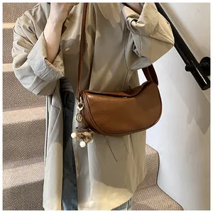Brown lychee leather half-moon crossbody bag with knit charm on a model in beige coat