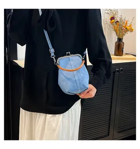 Detail of light blue denim shell bag with brown top handle worn as a crossbody purse