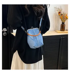 Close-up of blue denim shell bag featuring a kiss-lock closure and brown round handle