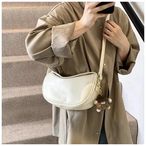 Close-up of beige moon-shaped hobo bag with leather texture and plush bear charm